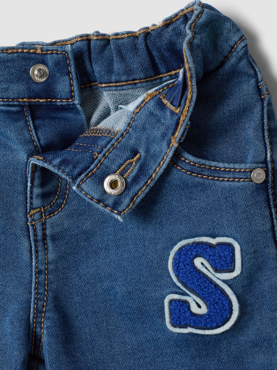 Jeans blu in cotone elasticizzato con applicazioni college per bimbo_2